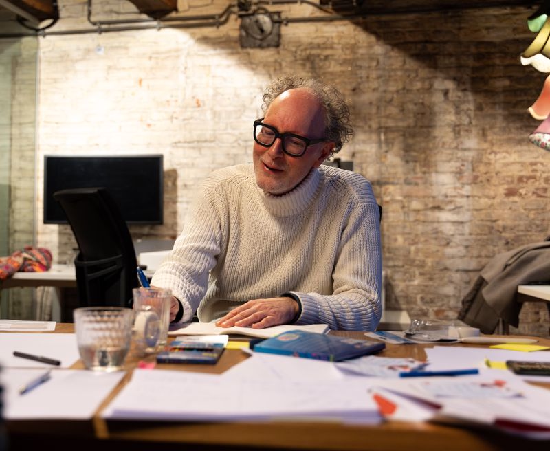 Een deelnemer in een witte trui lacht aan een werktafel vol aantekeningen