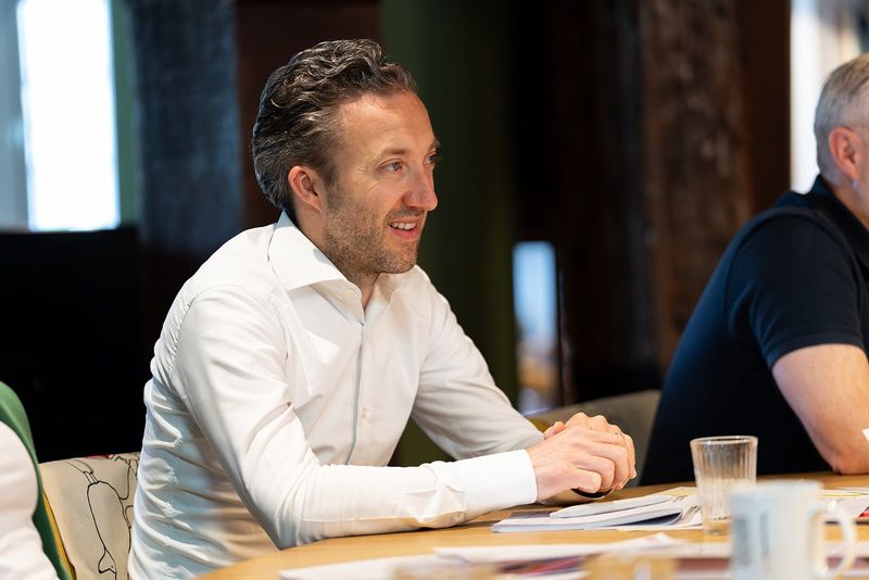 A participant in a white shirt listens and laughs at a table