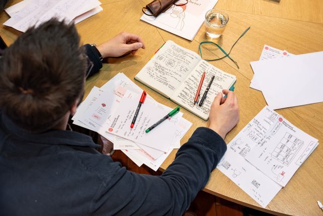 A participant takes notes in a notebook among the worksheets
