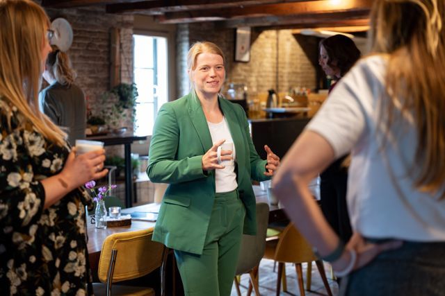 A woman in a green suit stands talking with participants