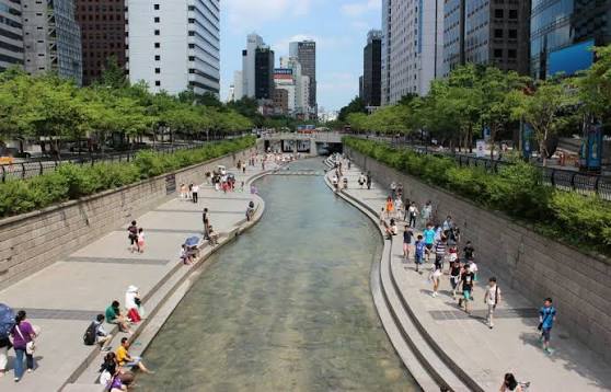 The Cheonggyecheon stream at night — lit stone walkways alongside the water, crowded with visitors where the motorway used to carry traffic