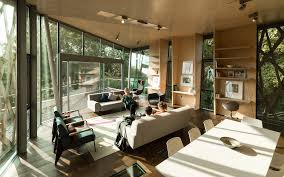 The open common room of a Maggie's Centre, with glass walls on two sides, a long table and natural light streaming through the trees outside