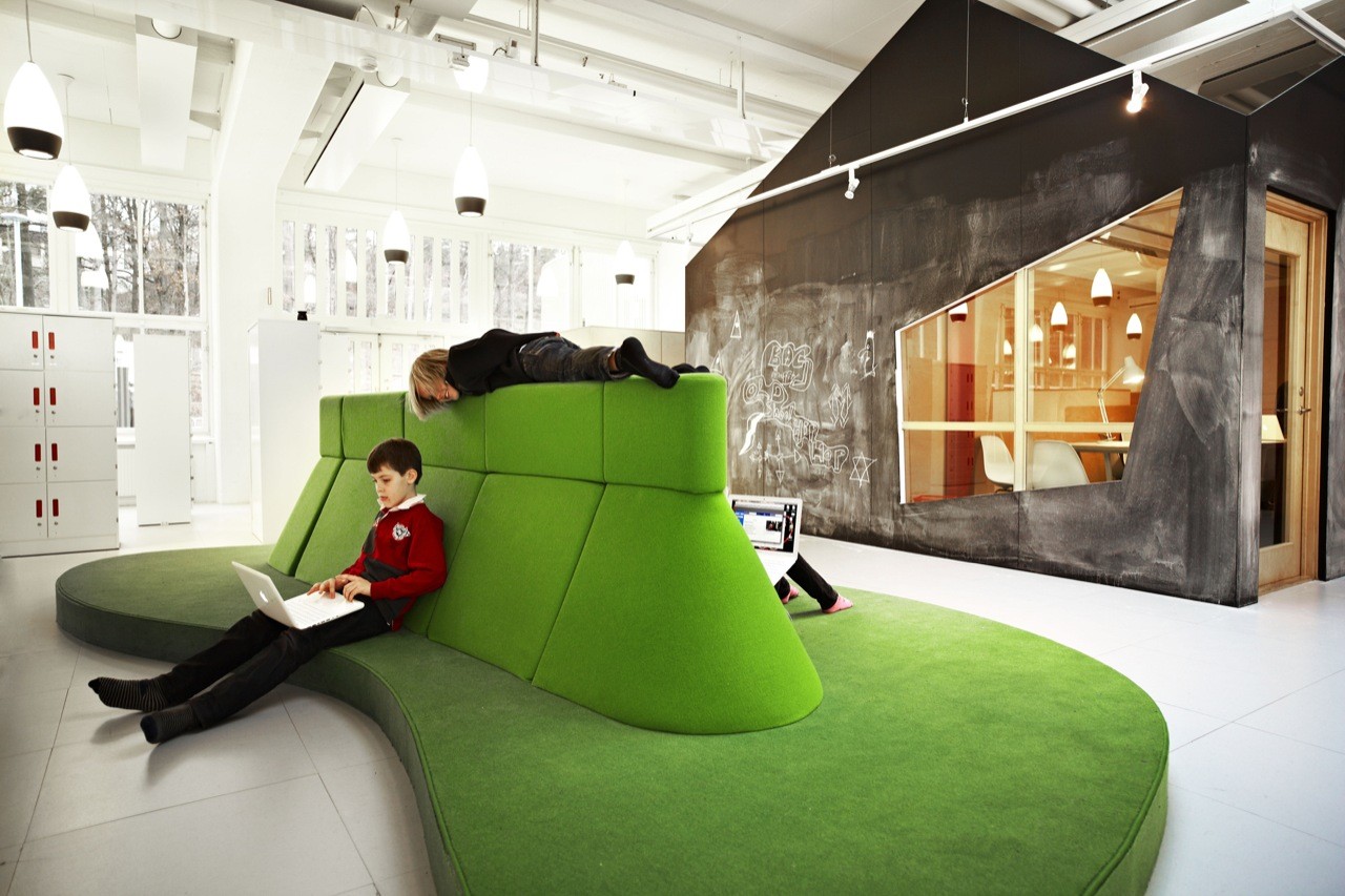 A child reading on the green landscape sofa at Vittra Telefonplan, next to the chalkboard cave classroom