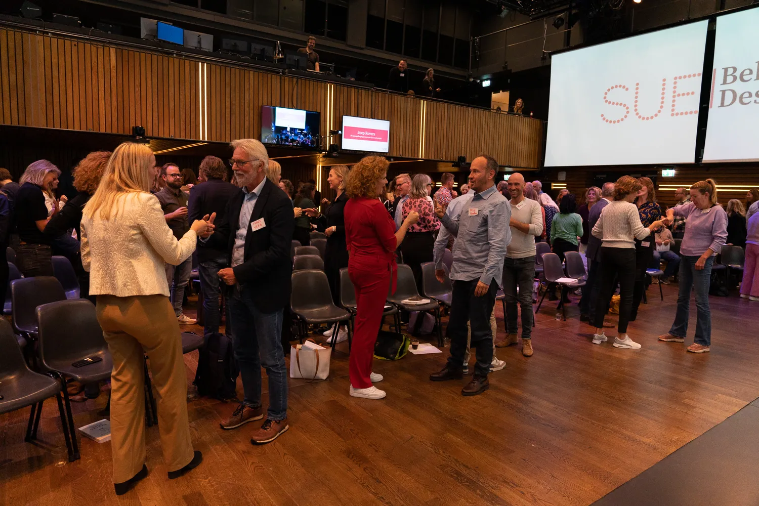 Deelnemers netwerken tussen de stoelen tijdens een pauze van het Behavioural Design Fest