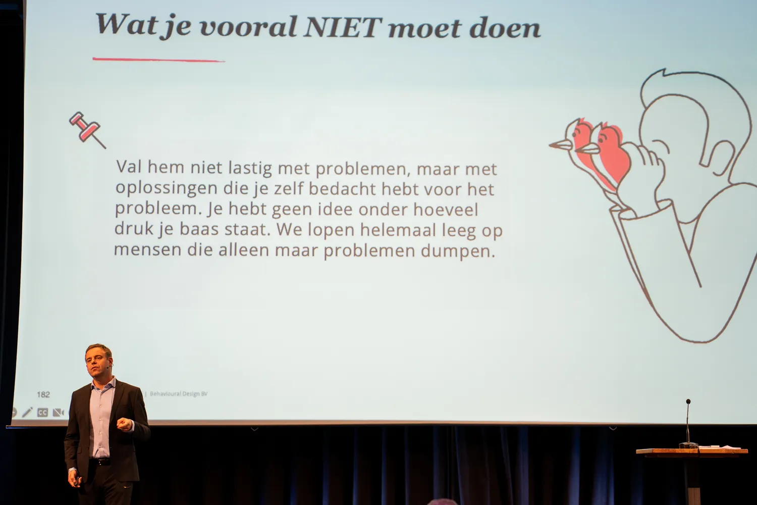 Presentatie op het podium van het Behavioural Design Fest met een SUE-illustratie op het scherm