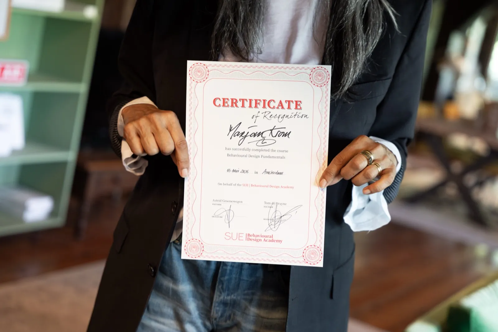 Deelnemer toont het certificaat van de training Behavioural Design Fundamentals, ondertekend door Astrid Groenewegen en Tom de Bruyne