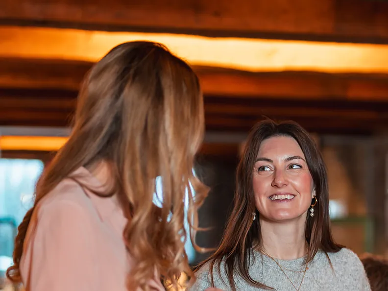Smiling woman talking to someone with their back to the camera, under wooden beams