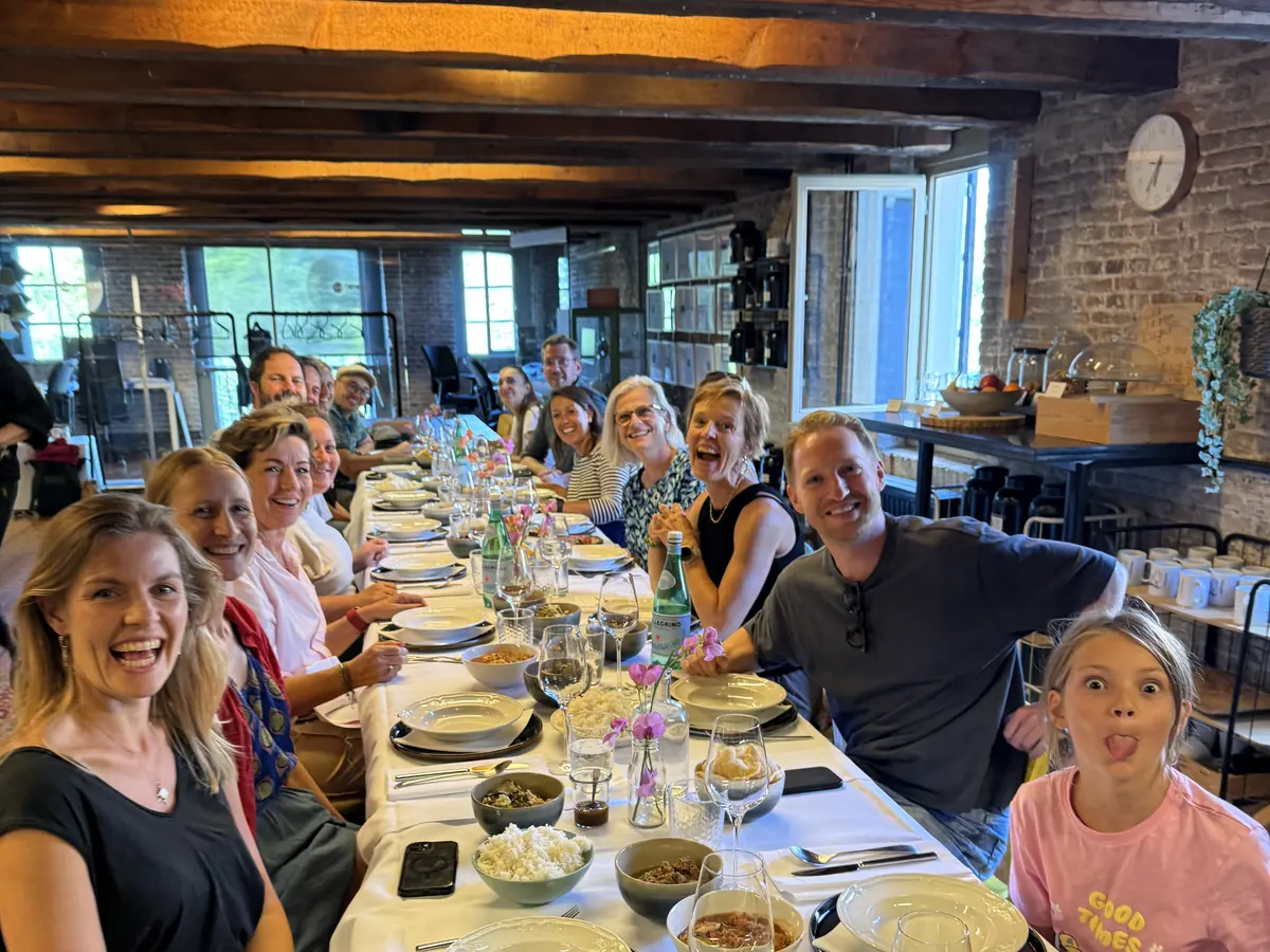 A group of adults and children at a laid long table under wooden beams