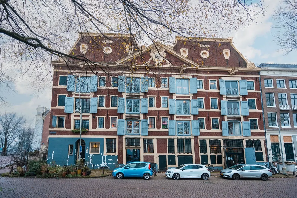 Gevel van het pand aan het 's-Gravenhekje met blauwe luiken en bomen langs het water