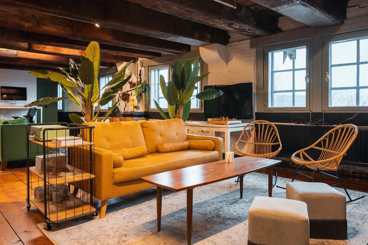 Lounge met gele bank, rotan stoelen en planten voor grote ramen