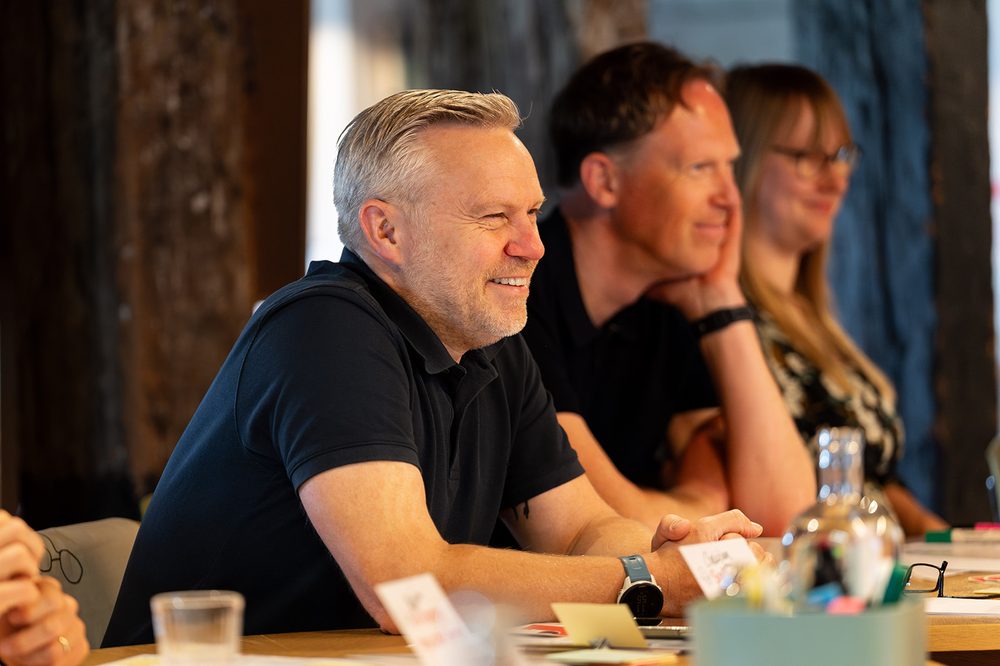 Drie deelnemers aan de trainingstafel in Amsterdam, geconcentreerd in gesprek met de trainer.