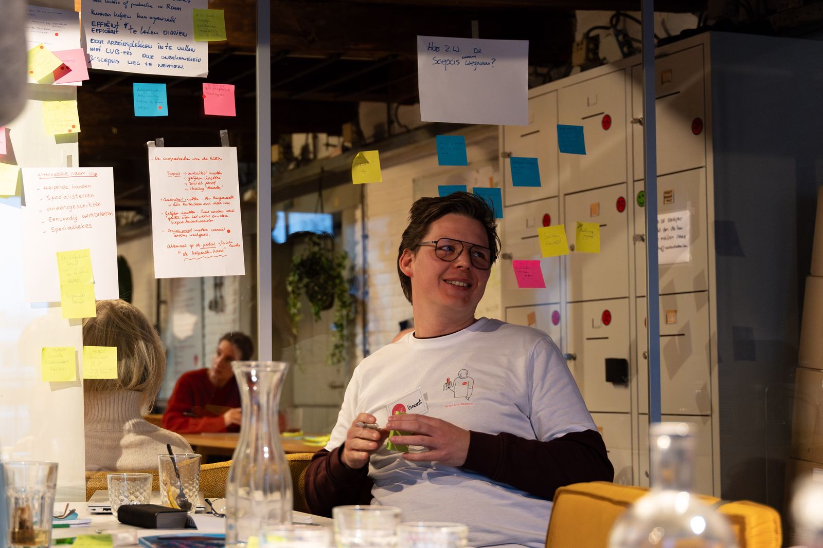 A participant laughing at a table in front of a wall of sticky notes during a session at SUE in Amsterdam